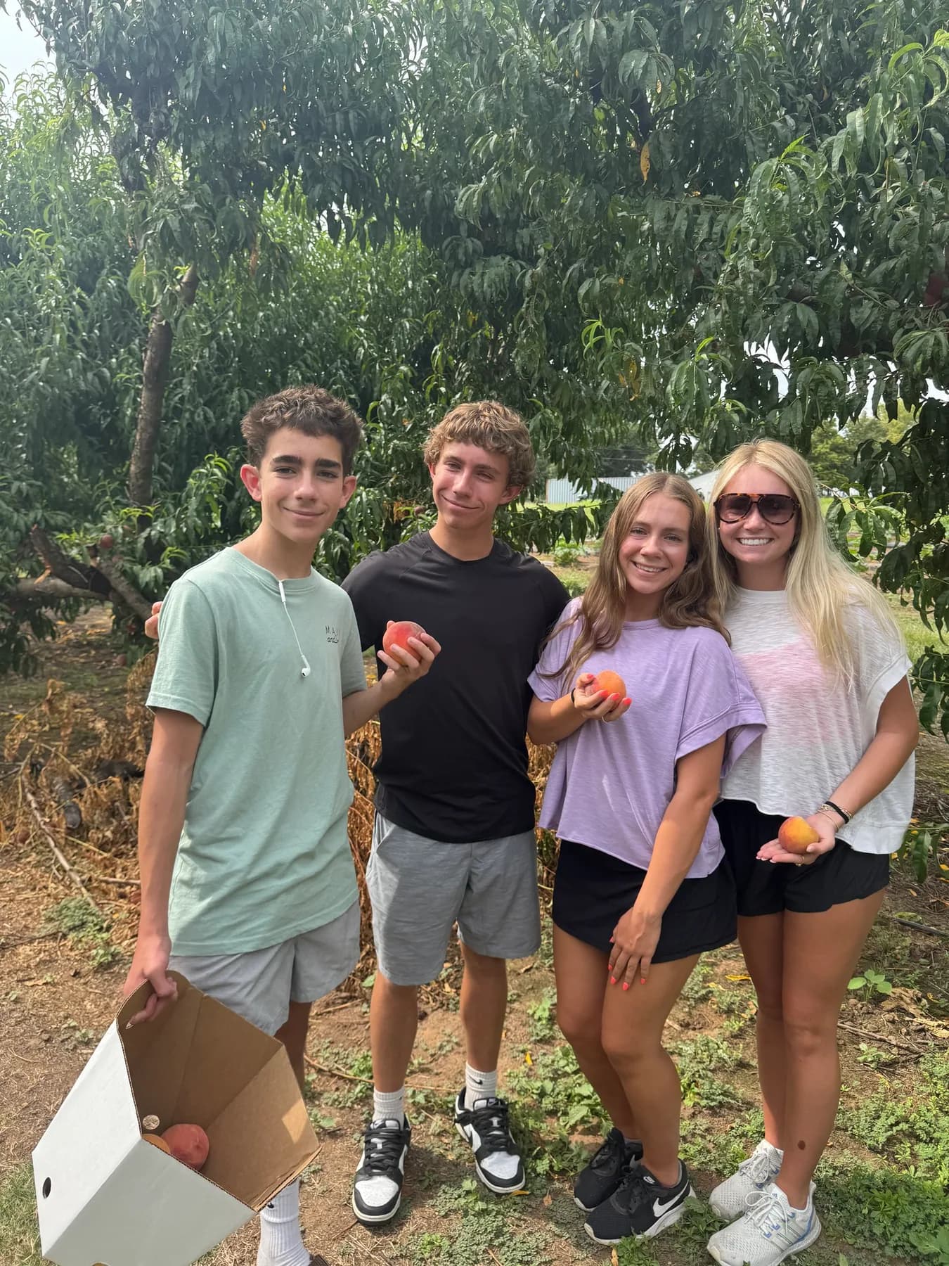 Group of visitors holding peaches in a Maine orchard.
