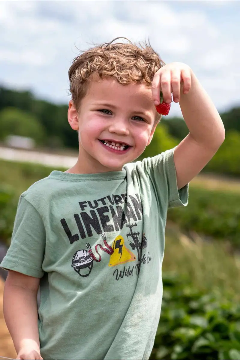 Child holding a fresh strawberry in a field for Massachusetts u-pick strawberry planning.