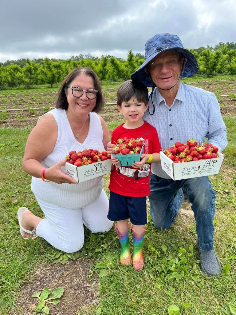 Family kneeling with baskets of strawberries — seasonal farm visit imagery.